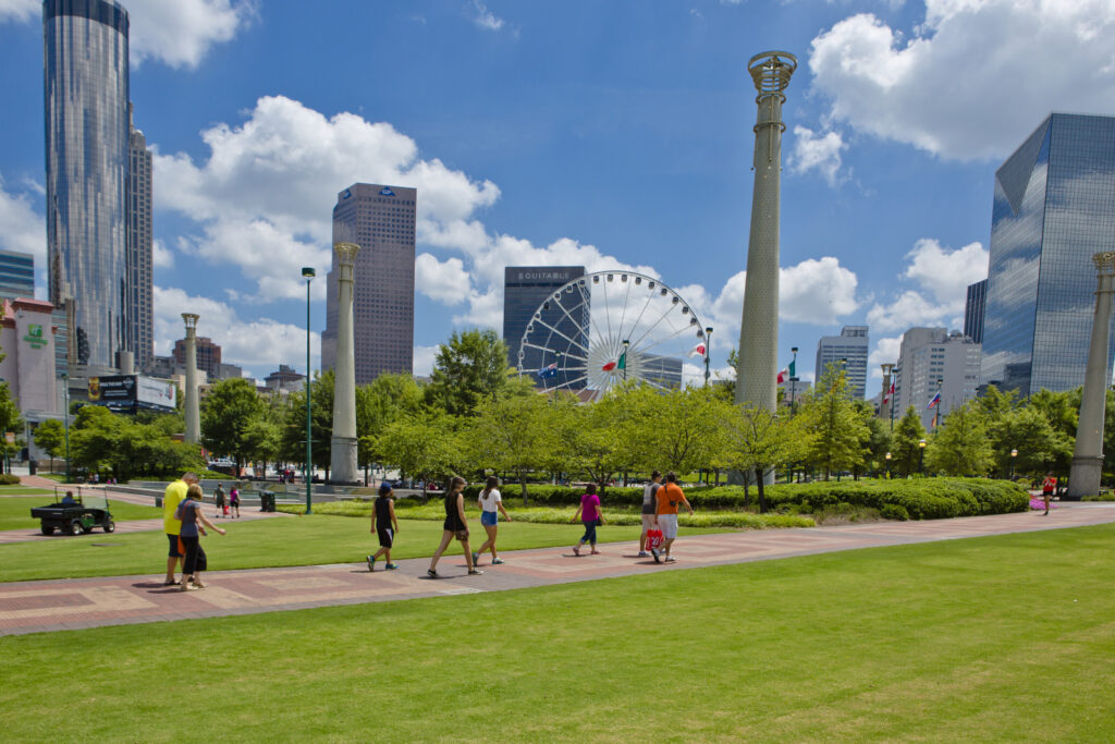 park with skyscrapers behind green grass trees and path with people walking